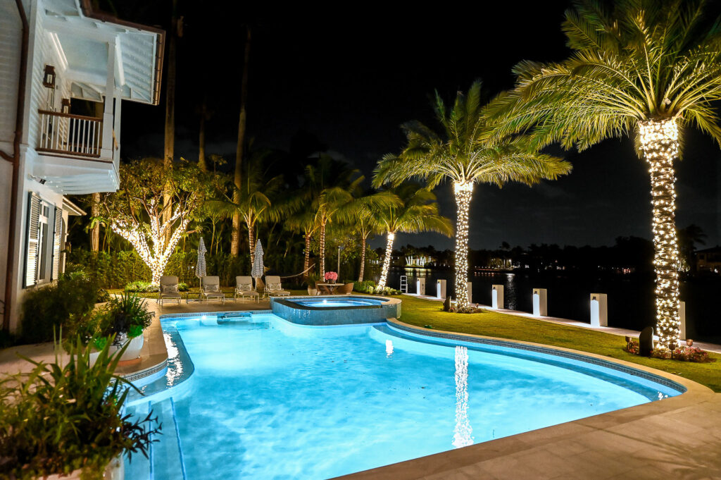 Luxurious holiday-style lighting installation on backyard palm trees of a high-end modern house with dock and water access in South Florida