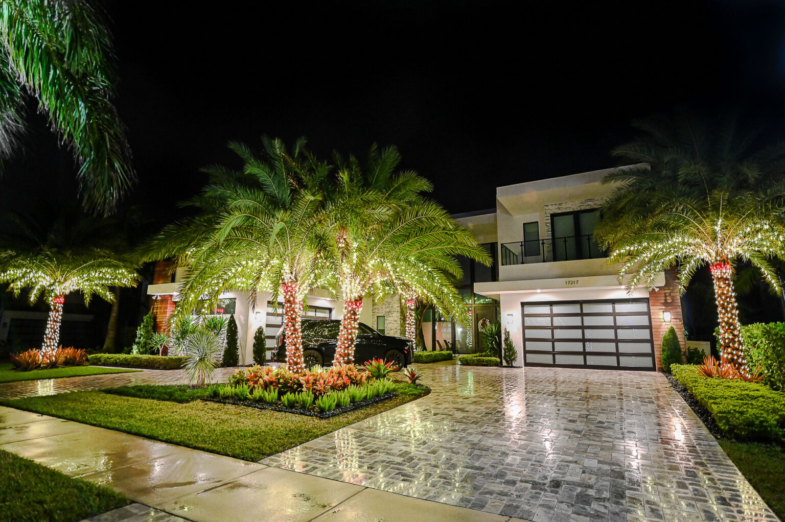 Modern home in Boca Raton, Florida, with five small palm trees in the front yard adorned with high-end holiday lighting installations