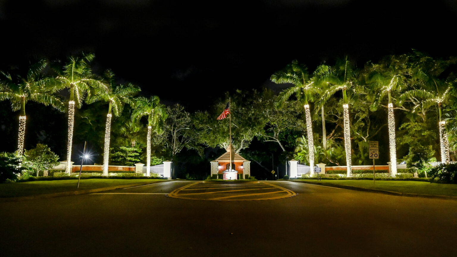 Stunning community entrance with symmetrically decorated royal palm lit up by premium quality Christmas-style lights wrapped around the tall palms beside the community entrance