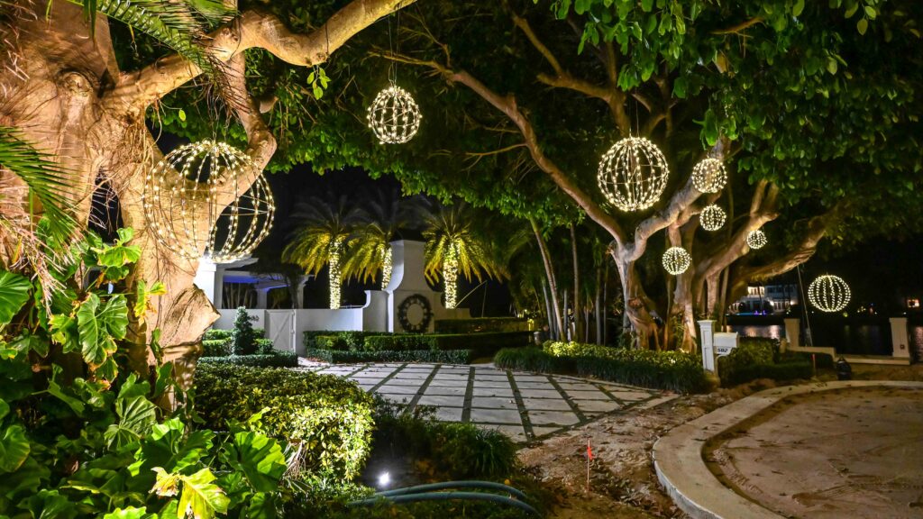 Luxurious South Florida Home entrance made up of a vegetation archway decorated with multiple hanging holiday light balls.