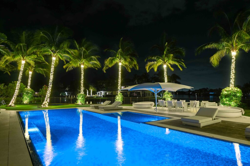 Poolside area with palm trees decorated in holiday-style lighting installation. Used for Hotel Lighting Landing page